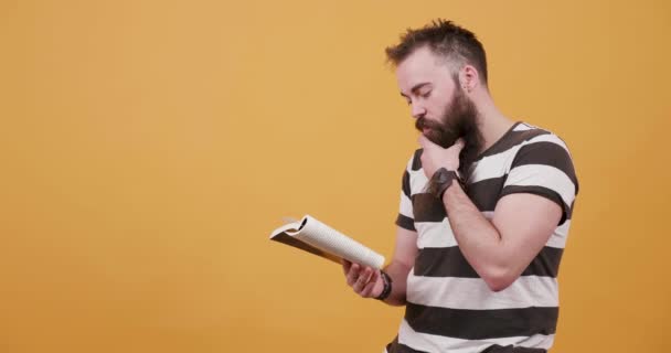 Joven leyendo silenciosamente un libro y acariciando su barba y bigote — Vídeo de stock