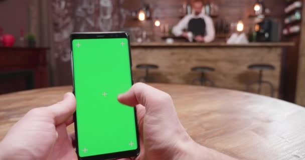 Handheld shot of man using a green screen phone in vintage pub — Stock Video