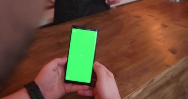 Bardaki adam karşı yeşil ekran ile bir telefon tutar