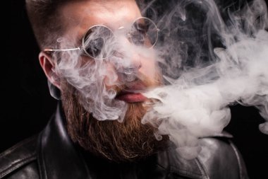 Arka plan üzerinde sigara duman exhaling güneş gözlüğü ile sakallı genç adam portresi kadar yakın