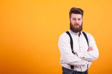 Sarı arka plan üzerinde kameraya ciddi seyir yakışıklı sakallı adam kollarını ile geçti