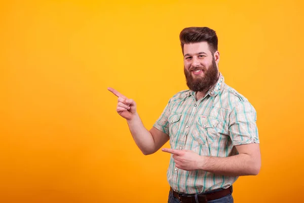 Hipster bärtiger Mann lächelt und zeigt auf gelben Hintergrund. — Stockfoto