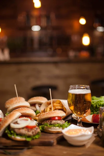 Tasty different burgers and a glass of cold beer on wooden table — Stock Photo, Image