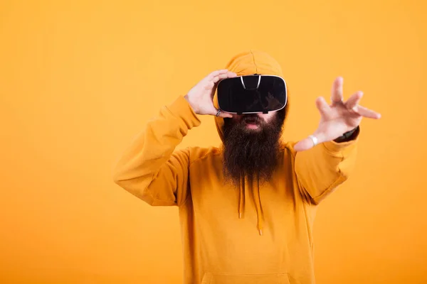Barbuto uomo indossa realtà virtuale auricolare allungando con la mano su sfondo giallo — Foto Stock