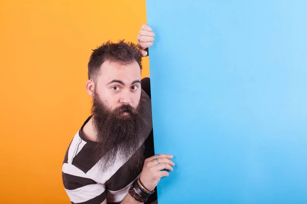 Homme attrayant avec une longue barbe tenant un espace de copie bleu portant t-shirt rayé sur fond jaune . — Photo