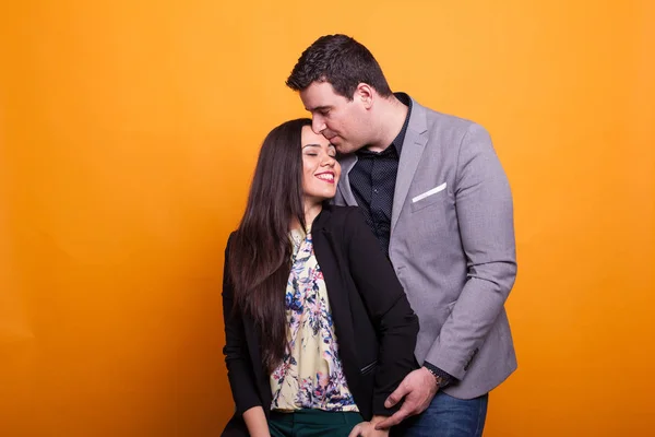 Husband kissing his wife forehead over yellow background.