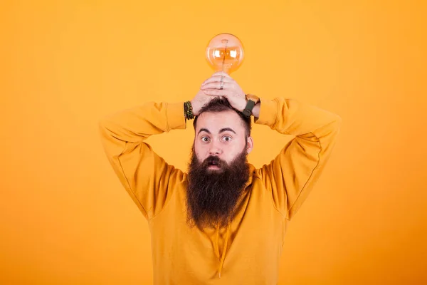 Engraçado barbudo homem com uma lâmpada sobre a cabeça na frente sobre fundo amarelo — Fotografia de Stock