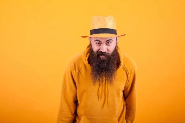 Porträt eines gutaussehenden bärtigen Mannes mit orangefarbenem Hut, der vor gelbem Hintergrund fasziniert in die Kamera blickt — Stockfoto