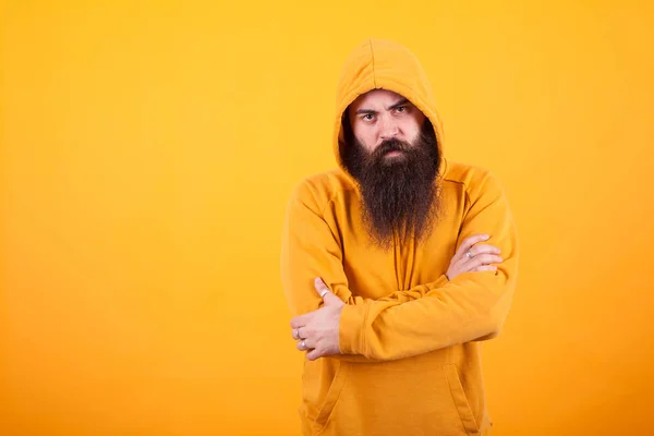 Portrait of dangerous man with long beard wearing a hoodie over yellow background — Stock Photo, Image