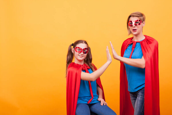 Mother and daughter dressed like superheros giving hi5 over yellow background.