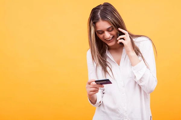 Mooi meisje glimlachend terwijl praten aan de telefoon en creditcard bedrijf over gele achtergrond — Stockfoto