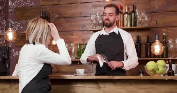 Barman nettoie un verre et écoute très concentré à son collègue féminin — Video
