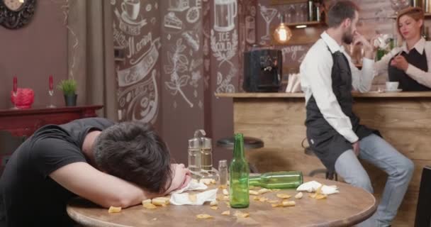 Молодой бармен пытается разбудить пьяного клиента — стоковое видео