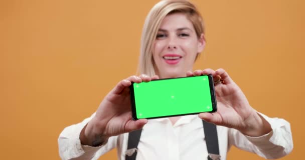 Ξανθιά γυναίκα πάνω από το κίτρινο φόντο που κρατούν στα χέρια της ένα smartphone με πράσινη οθόνη — Αρχείο Βίντεο