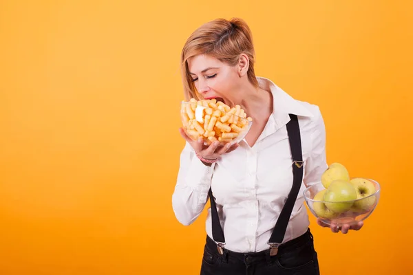 Pretty blond woman with short hair taking a bite from her corn puffs over yellow background. — Stock Photo, Image