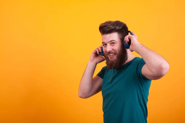 Hombre barbudo guapo con auriculares azules en camiseta verde mirando a la cámara sobre fondo amarillo —  Fotos de Stock