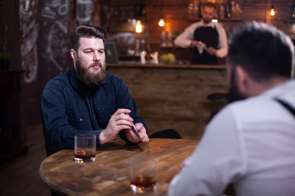 Hombres barbudos guapos jugando a las cartas en un pub y bebiendo whisky —  Fotos de Stock