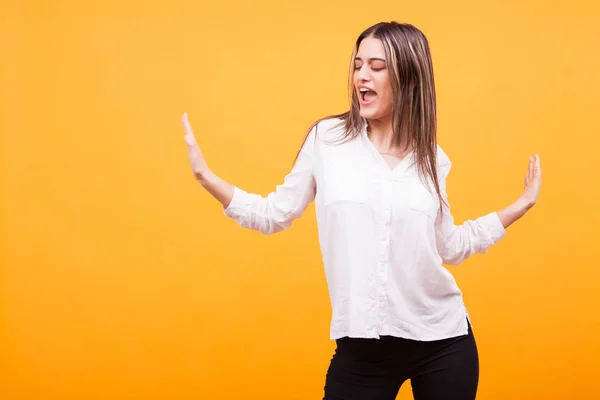 Porträtt av vacker ung kvinna som dansar och sjunger över gul bakgrund — Stockfoto