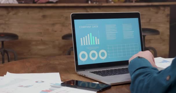 Чоловік сидить за столом кав'ярні і дивиться на графіки даних компанії і діаграми — стокове відео