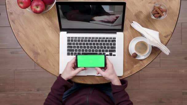 Hombre en la cafetería mira un video y sostiene el teléfono inteligente con pantalla verde en — Vídeos de Stock