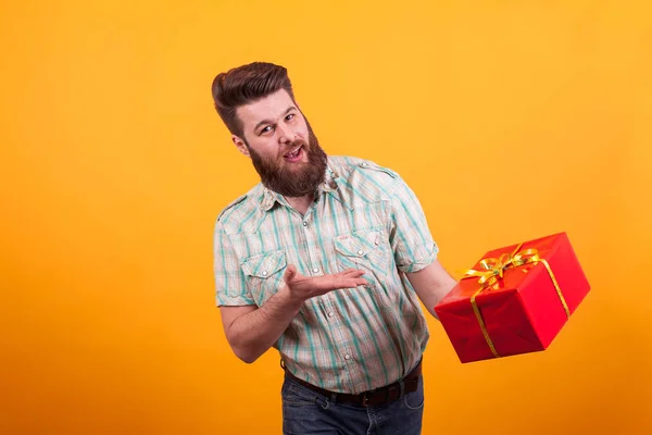 Homme barbu joyeux tenant une boîte cadeau d'anniversaire sur fond jaune . — Photo