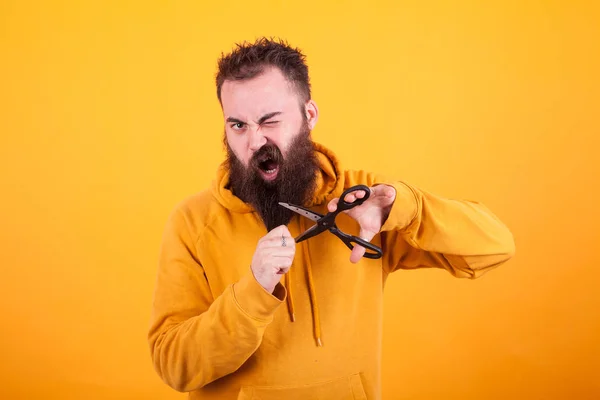 Freddo uomo barbuto cercando terrorizzato mentre si taglia la barba su sfondo giallo — Foto Stock