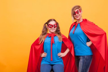Youn anne ve küçük kızı sarı arka plan üzerinde superheros kırmızı pelerin giyiyor