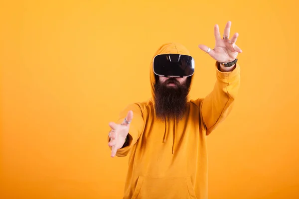 Jovem atraente com barba longa vestindo fone de ouvido realidade virtual fazendo gestos de mão sobre fundo amarelo — Fotografia de Stock