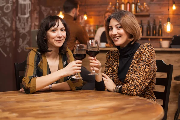 Schöne junge Frauen, die ein Glas Rotwein trinken und in die Kamera lächeln — Stockfoto