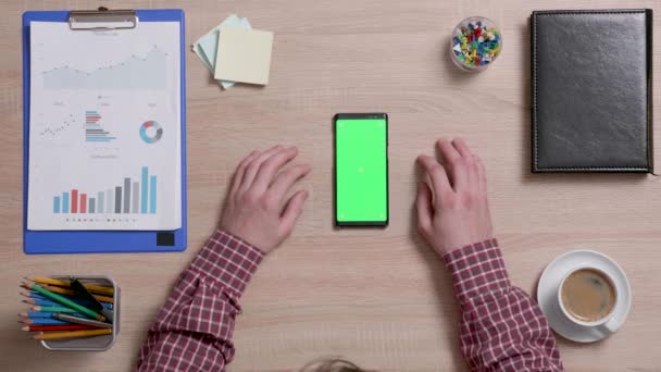 Vista superior de mãos masculinas e um telefone inteligente com tela verde em uma mesa de escritório de madeira — Vídeo de Stock