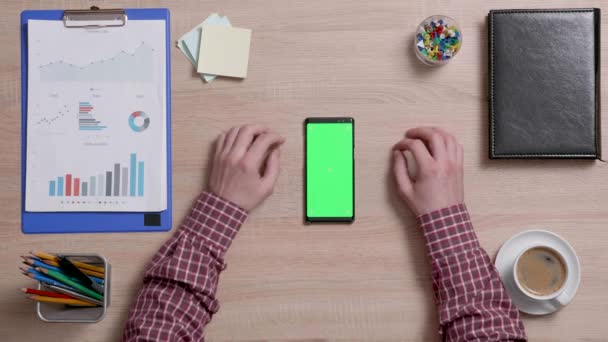 Visão superior de mãos masculinas rolando na borda esquerda de um telefone inteligente com tela verde em — Vídeo de Stock