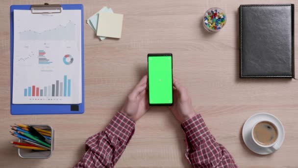 Vista superior de um homem mãos segurando seu smartphone e olhando para uma tela verde . — Vídeo de Stock