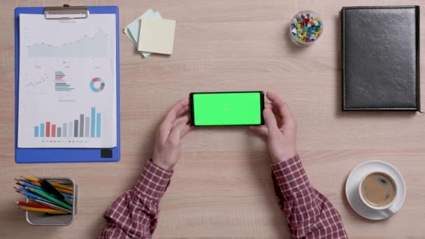 Чоловічі руки над офісним столом, що тримає смартфон із зеленим екраном — стокове відео