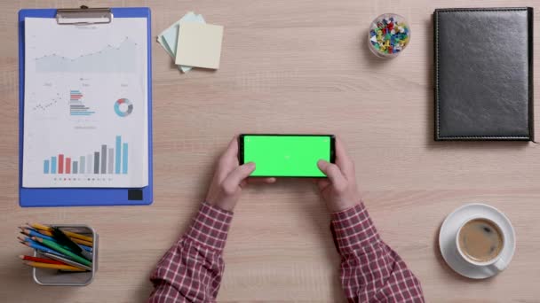 Ман вручает офисный стол, чтобы начать играть в игру на смартфоне с зеленым экраном — стоковое видео