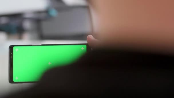 Revealing over the shoulder shot of a green screen on a smartphone — Stock Video