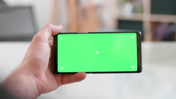 Mão de homem segurando o smartphone horizontalmente com tela verde em — Vídeo de Stock