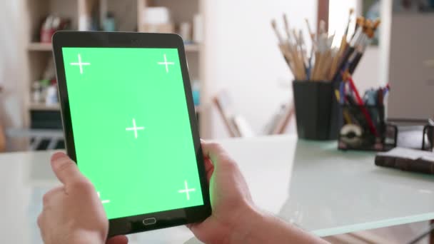 Joven artista mira una pantalla verde tabletas en su estudio — Vídeo de stock