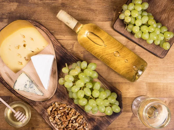 Верхний вид на бутылку белого вина рядом со свежим виноградом на деревянном столе . — стоковое фото