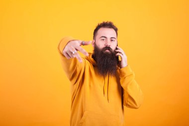 Serin sakallı adam kameraya bakıyor ve sarı arka plan üzerinden telefonda konuşuyor