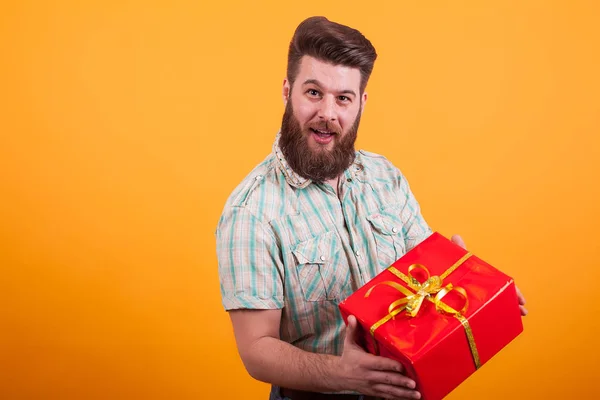 Jeune homme barbu tenant une boîte-cadeau rouge et regardant la caméra sur fond jaune — Photo