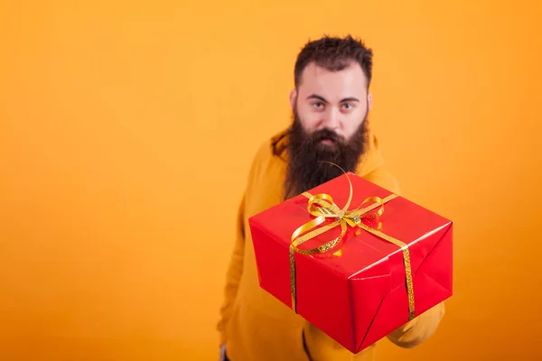 Atractivo hombre barbudo con capucha amarilla zapatos caja de regalo roja sobre fondo amarillo . —  Fotos de Stock