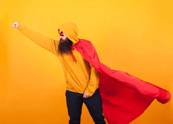 Bebaarde hipster gekleed in superheld kostuum vliegen weg te slaan van de wereld ovr gele achtergrond — Stockfoto