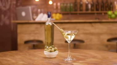 Tahta bir masada zeytinli bir şişe ve bir bardak martini