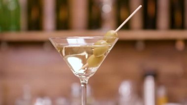 Zeytinle süslenmiş martini camının paralaks çekimini yakınlatın