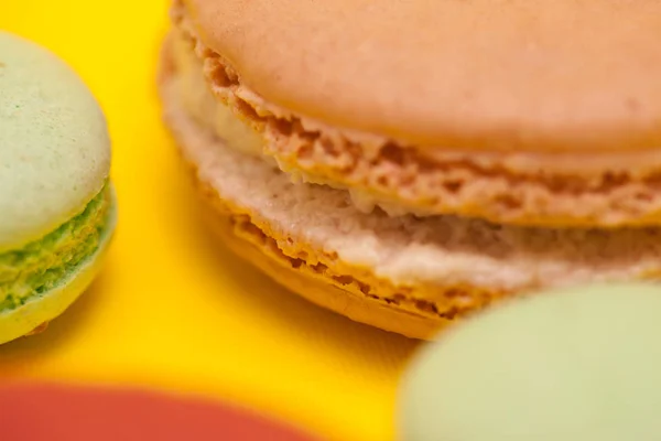 Close-up grote Macaroon karamelsmaak naast weinig bitterkoekjes over gele achtergrond — Stockfoto