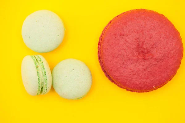 Grote zoete frambozen Macaron naast weinig bitterkoekjes over gele achtergrond — Stockfoto