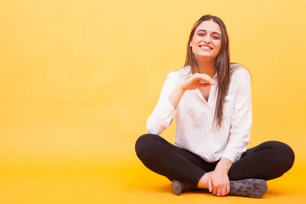 Mooi meisje glimlachend naar de camera in Studio en zittend over gele achtergrond — Stockfoto