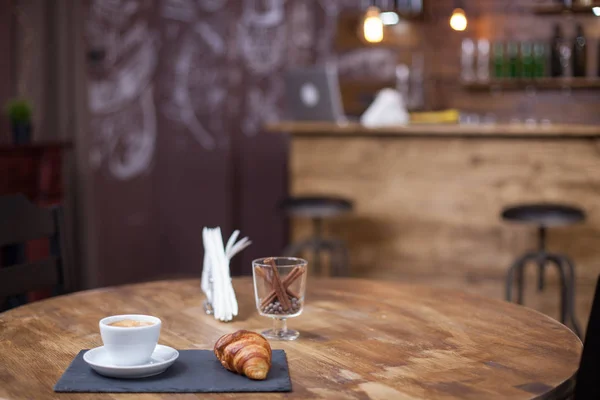 Tasse de café savoureux à côté de délicieux croissant servi sur une assiette noire lapidée — Photo