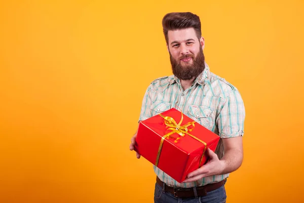 Jeune homme barbu regardant la caméra et tenant une boîte cadeau sur fond jaune — Photo