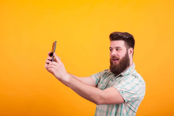 Hipster bärtiger Mann mit einem Videoanruf auf seinem Handy vor gelbem Hintergrund — Stockfoto